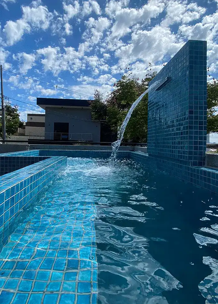 piscina em L com prainha e revestimento de vidro azul