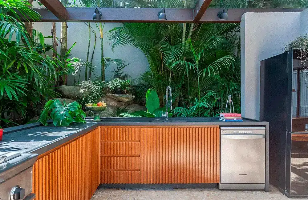 espaço de churrasqueira com painel ripado e muitas plantas no paisagismo 