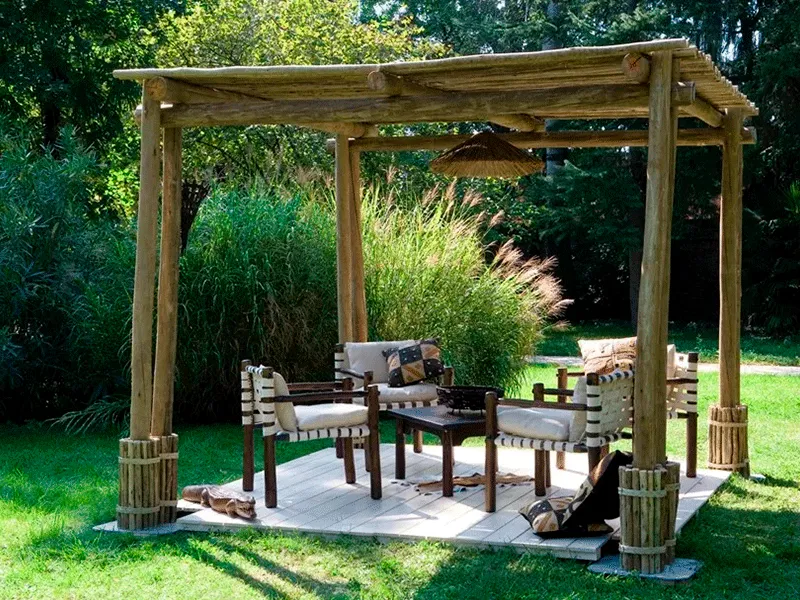 Pergolado no meio do jaridm com plantas e móveis de decoração