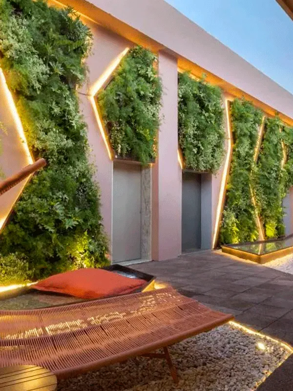 Espaço com revestimento externo amadeirado e jardim vertical com luzes de led em volta destacando sua compocisão do paisagismo