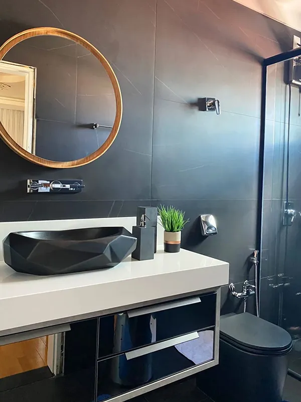 lavabo com revestimento preto na parede com espelho redondo sendo destacado