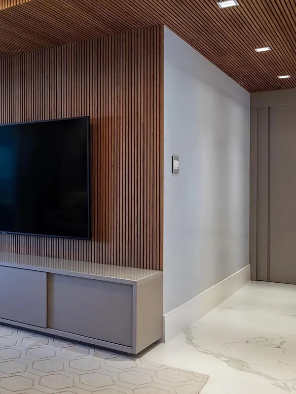 durabilidade garantida na sala com porcelanato no piso e uma parede de painel ripado de madeira complementando o painel da tv