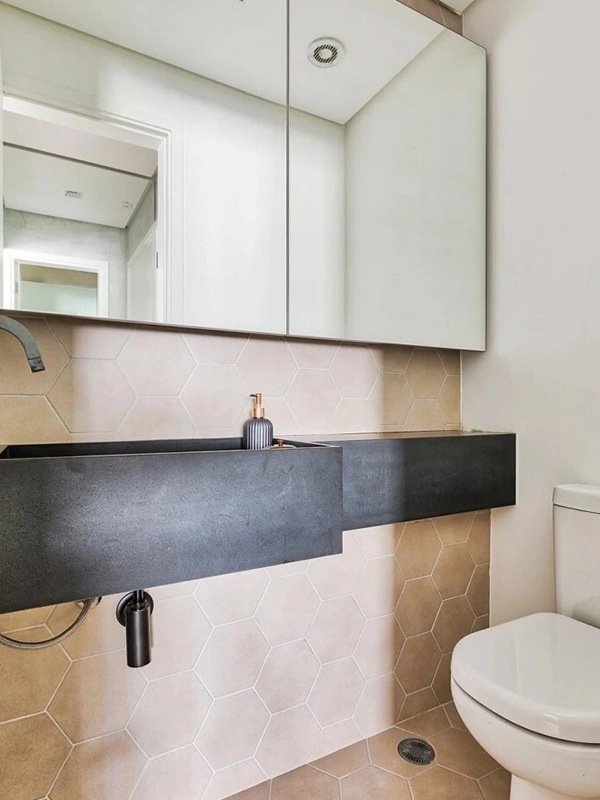 bancada preta destca a ceramica marrom na parede do banheiro com espelho que expande o local 
