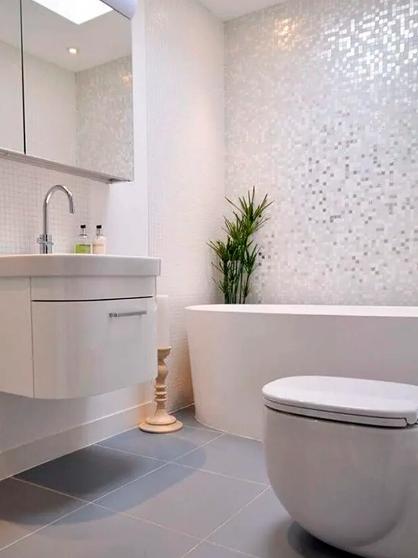 Banheiro moderno com banheira independente, pia flutuante com pia e vaso sanitário, decorado com mosaicos e um vaso de planta.