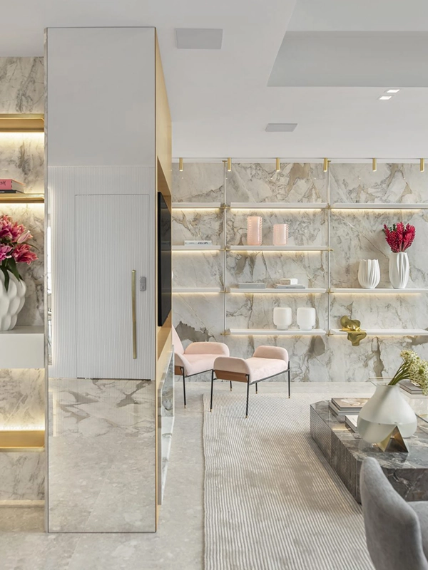 Uma luxuosa sala de estar moderna com paredes de mármore branco, um tapete cinza macio, prateleiras com detalhes dourados e elegantes arranjos florais.