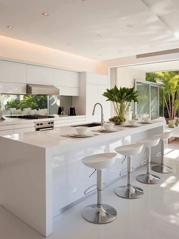 Cozinha moderna com armários brancos, revestimento branco na ilha central com bancos altos e ampla janela que permite a entrada de luz natural.