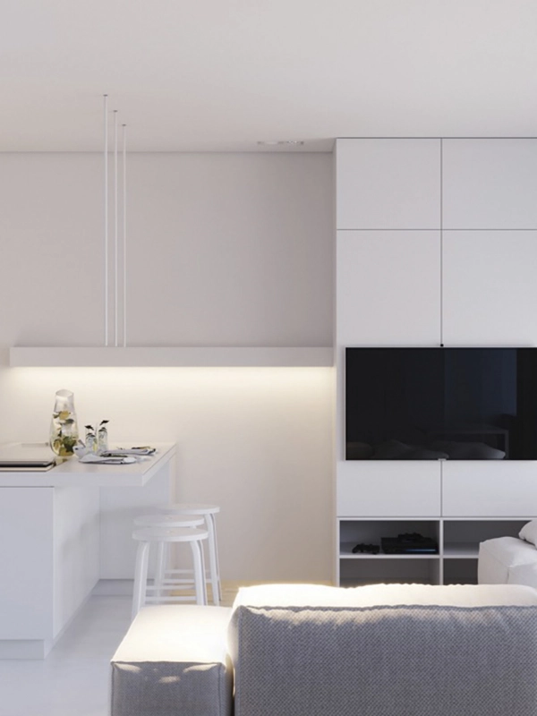 Sala minimalista com revestimento branco, pequena kitchenette, TV de parede e iluminação suave.