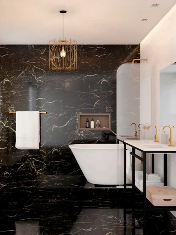 Banheiro luxuoso com paredes de mármore preto e piso em revestimento preto, banheira independente branca, luminária pendente dourada e móveis minimalistas.