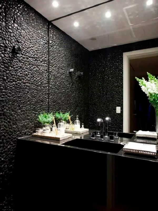 Banheiro moderno com revestimento texturizado preto, bancada preta com duas pias, plantas verdes e acessórios espelhados.