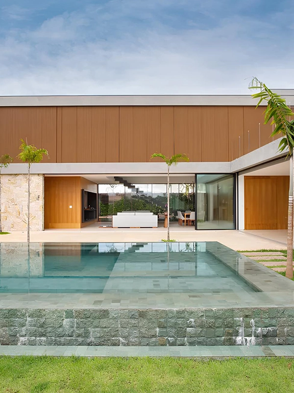 Área externa com piscina com revestimento azul que destaca a fachada da casa que contem painel ripado de madeira 