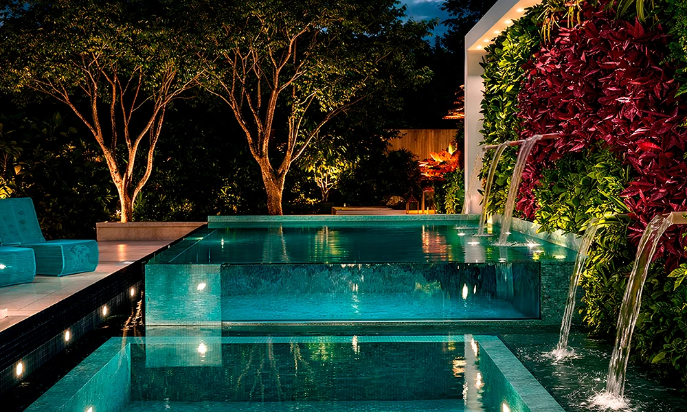Piscina externa moderna à noite com elementos aquáticos iluminados, uma parede de jardim vertical com plantas exuberantes para piscina e árvores ao redor, criando um ambiente tranquilo.